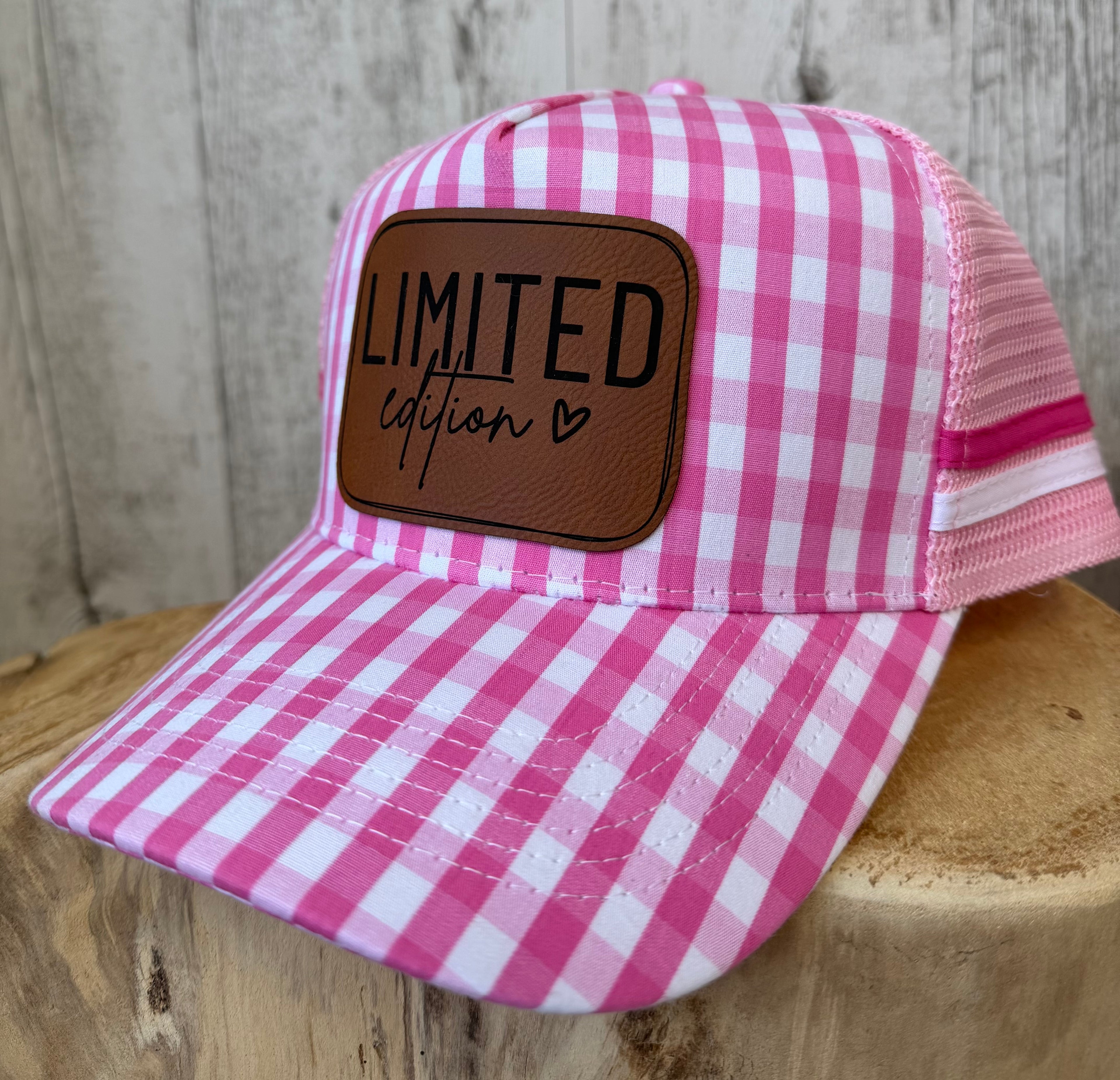 Pink and white gingham check trucker cap with brown leather Limited Edition patch on a wooden display