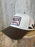 White trucker cap with dark brown brim, pink-backed embroidered Limited Edition patch and deer silhouette side badge on a wooden display
